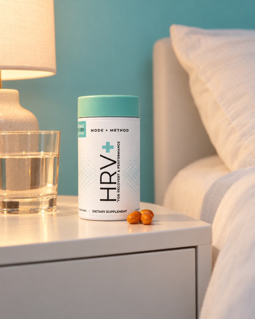 A bottle of Mode + Method HRV+ on a nightstand beside a glass of water and three orange softgels.